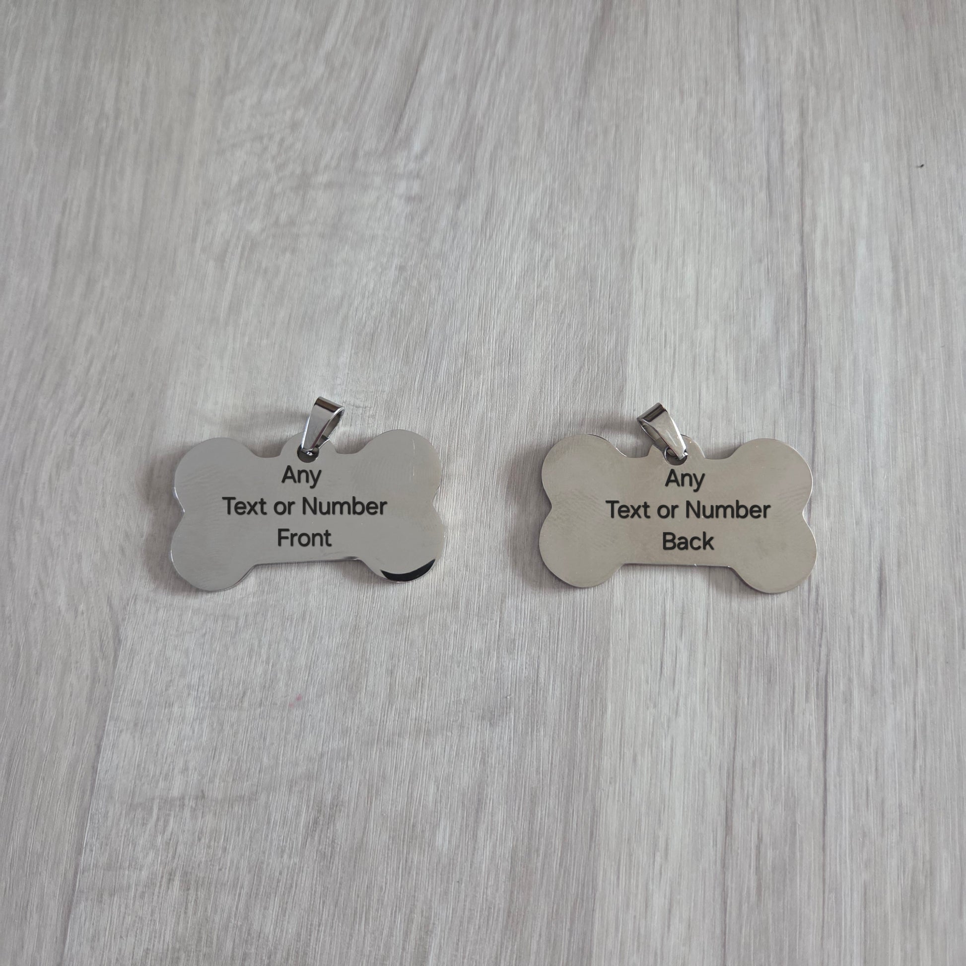 Two bone-shaped metal dog tags on a wooden surface