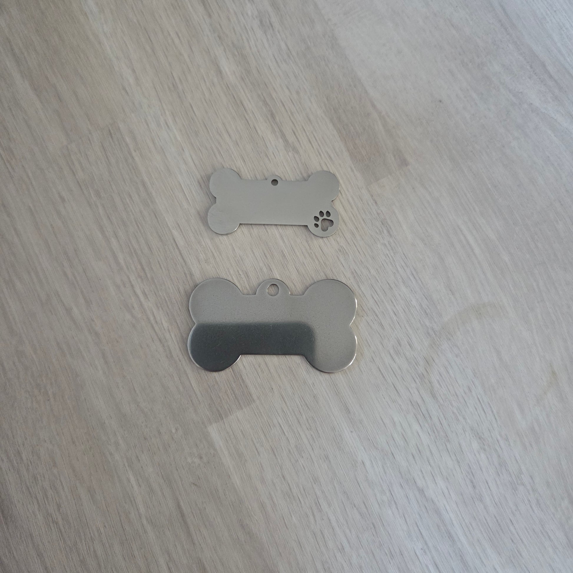 Two metallic dog tags shaped like bones on a wooden surface