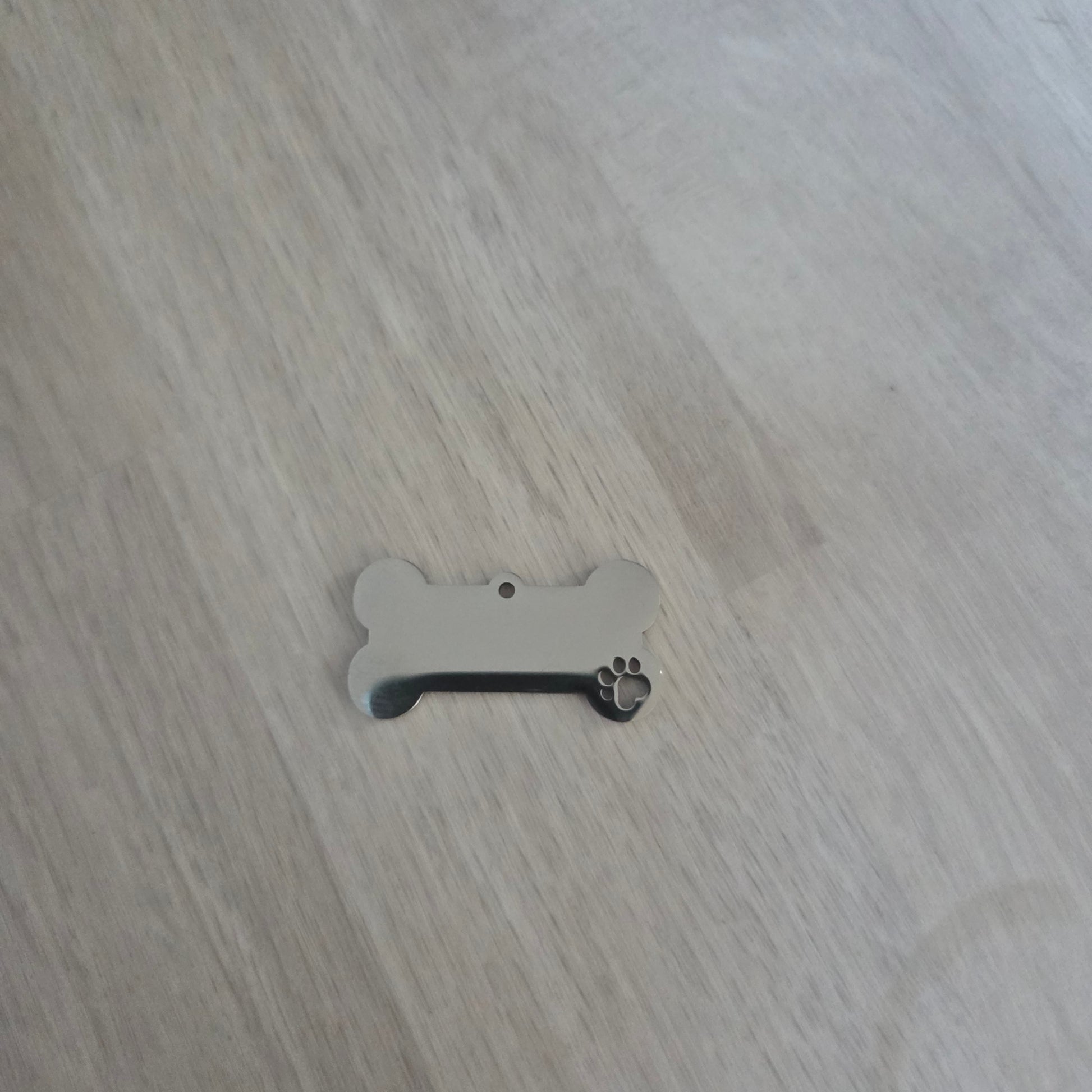 Metal dog tag shaped like a bone with paw print on a wooden surface